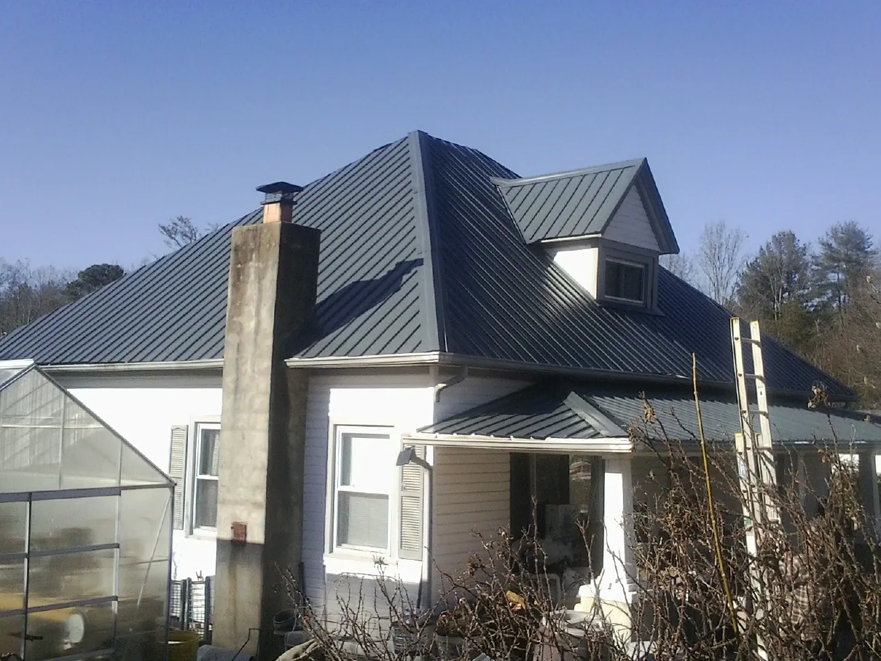 Dark blue standing seam metal roof on a white farmhouse with dormer — Slate & Tile Roof Repair by Roofing Brothers in West Fargo