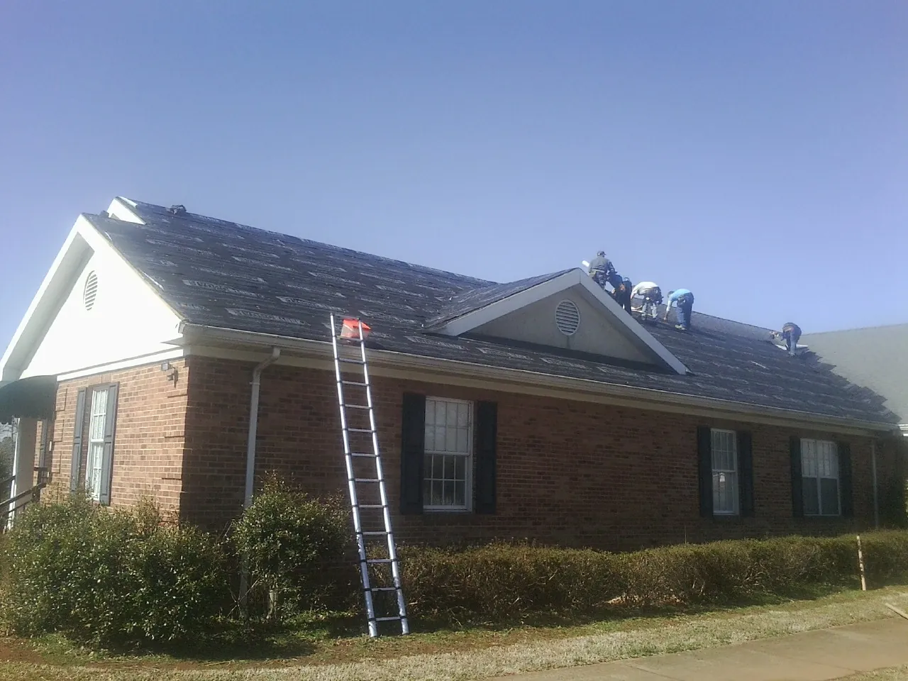 Crew tearing shingles off a brick ranch roof with a ladder set — Metal Roof Repair work by our crew in West Fargo