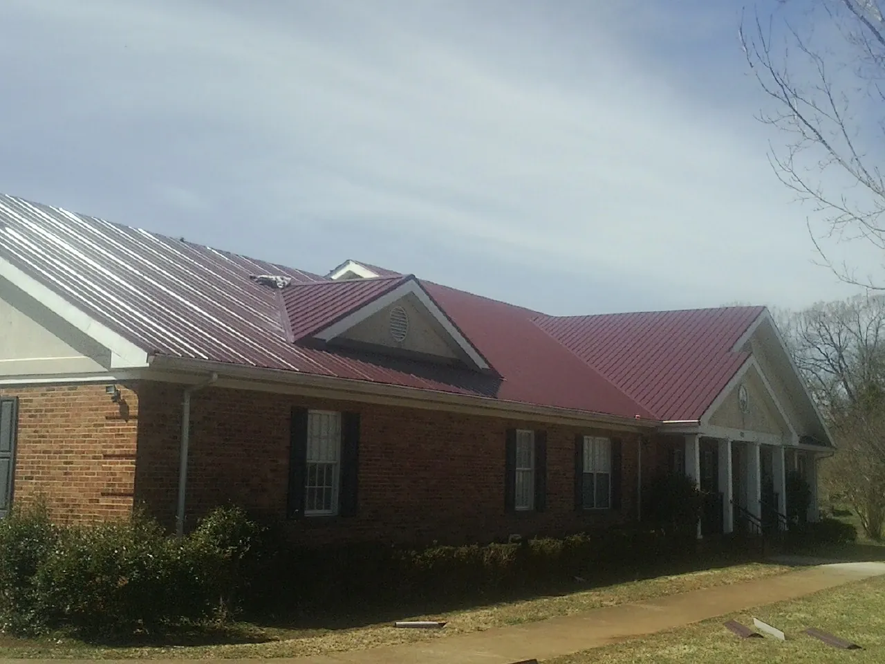 Red metal roof with gabled entries on a long brick building, from a Hail Damage Roof Repair job in West Fargo