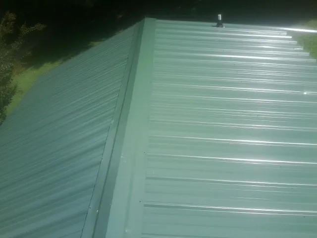 New green metal panels meeting at the ridge of a roof — Flat Roof Repair work by our crew in West Fargo