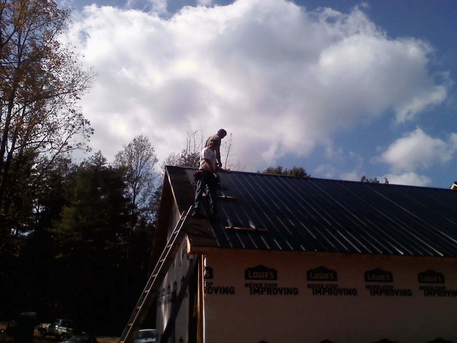 Roofer fastening dark metal panels high against a cloudy sky, from a Roof Inspection job in West Fargo