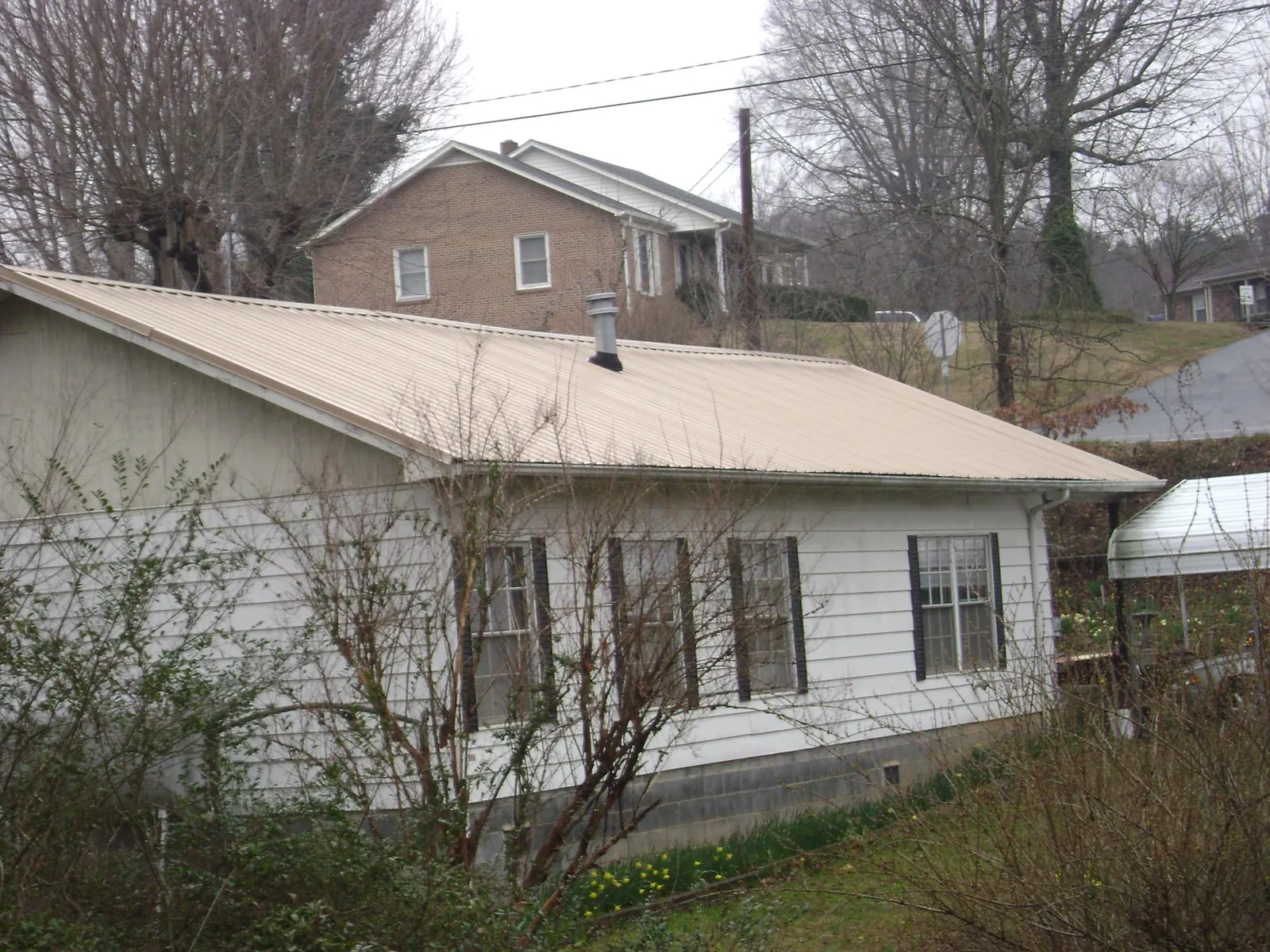 Tan metal roof on a white sided house set into a hillside — Commercial Roofing by Roofing Brothers in West Fargo